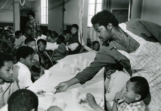 Charles Bursey hands plate of food to a child seated at Free Bre